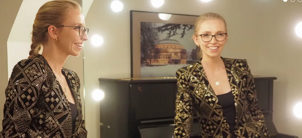 Anna Lapwood wearing a gold dress with a picture of the Royal Albert Hall behind her